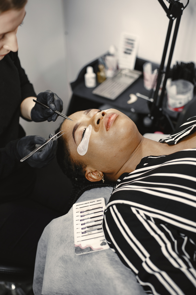 A Woman Putting Eyelash Extension to a Woman Lying on Bed